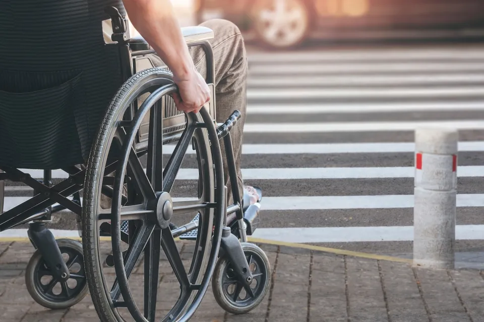 Close-up of man in manually operated wheelchair waiting at urban crosswalk.